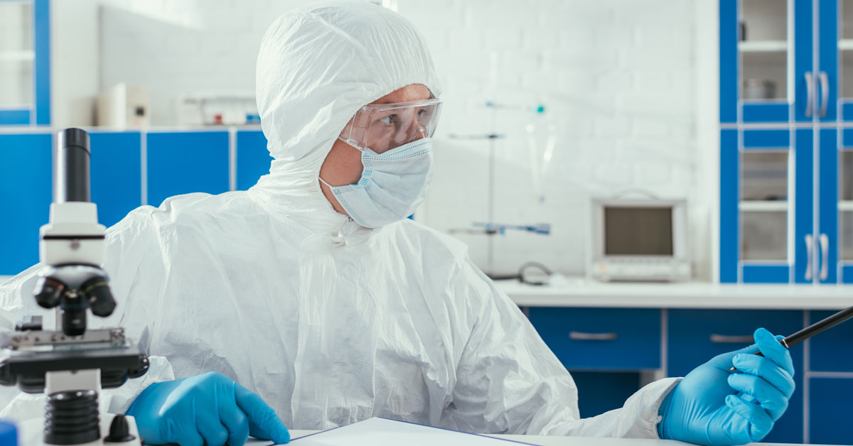 Biochemist in hazmat suit sitting near microscope
